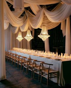 a long table is set up with white draping and hanging chandeliers