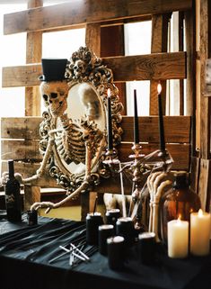 a skeleton sitting in front of a mirror surrounded by candles and other items on a table