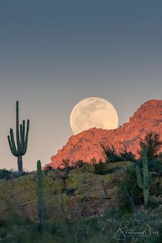 the full moon is setting over mountains and cactus