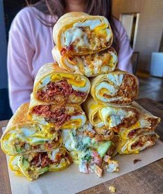 a stack of burritos sitting on top of a wooden table next to a woman