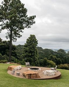 an outdoor fire pit surrounded by trees in the middle of a grassy area with benches and chairs around it