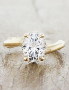 a yellow gold engagement ring with a round cut diamond in the center, on top of a wooden surface