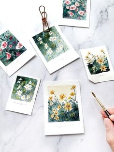 a person holding a brush near some cards with flowers on them and one has a pen in it