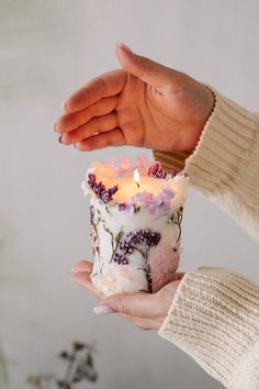 a person holding a lit candle in their hand with flowers all over the inside of it