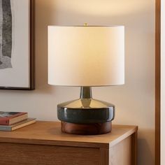 a table lamp sitting on top of a wooden dresser next to a book shelf and framed artwork