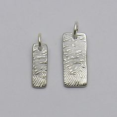 two small silver pendants with waves on them, one in the shape of a fingerprint