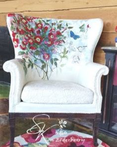 a white chair sitting in front of a fire place with flowers painted on the back