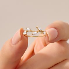 a woman's hand holding a gold ring with three leaves on it