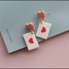 a pair of white and red earrings with hearts on them sitting on top of a pink surface