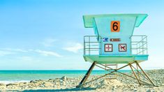 a lifeguard tower sitting on top of a sandy beach next to the ocean and blue sky