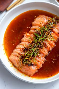 a white bowl filled with fish covered in sauce and garnished with green sprigs