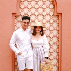 a man and woman standing next to each other in front of a wall with an arch