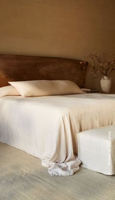 a bed with white sheets and pillows in a bedroom next to a vase filled with flowers