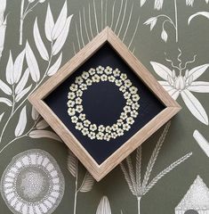 a wooden frame with white flowers in it on a wallpapered surface next to a black and white floral pattern