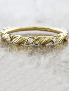 a yellow gold wedding band with three diamonds on the top and bottom, sitting on a marble surface