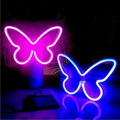 two neon butterflies sitting next to each other on top of a table in the dark