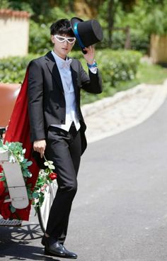 a man in a tuxedo is walking down the street with a hat on his head