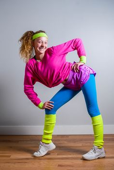 a woman in pink shirt and blue leggings standing on one leg with her hands behind her head