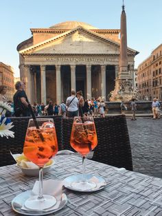 two glasses of wine sitting on top of a table in front of an old building