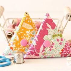 three triangle shaped pieces of fabric sitting on top of a table next to scissors and sewing needles