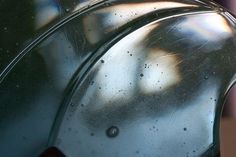 a close up view of a metal object with water droplets on it and a tree in the background