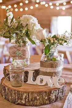 two mason jars filled with flowers are sitting on top of a wooden slice that says love