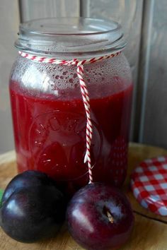 two plums sit next to a jar of juice