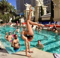 a woman doing a handstand in the middle of a swimming pool with other people