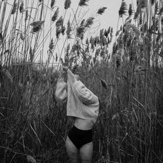 a woman standing in tall grass with her back to the camera