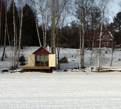 a small cabin in the middle of some snow covered land with trees and houses behind it