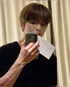 a young man taking a selfie with his cell phone in front of him and holding a piece of paper