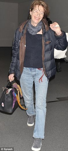 a woman walking through an airport with her hand in her pocket and holding two bags