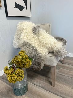 a white chair sitting next to a vase with yellow flowers in it on a hard wood floor