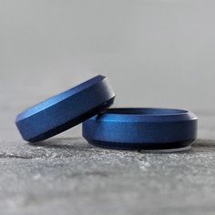 two blue wedding bands sitting on top of each other in front of a gray background