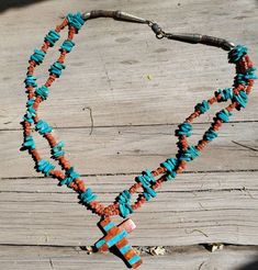 a long necklace with turquoise and orange beads on a wooden table next to a piece of wood