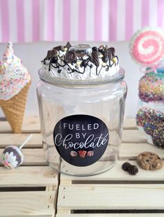 a glass jar filled with frosting and sprinkles on top of a wooden table