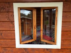 two windows are open on the side of a wooden building with a bed in it