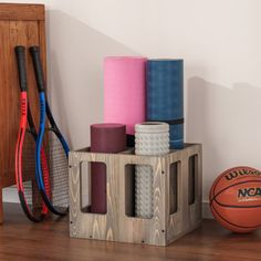 a basketball, racket, and other sports equipment sit on a wooden crate in front of a white wall