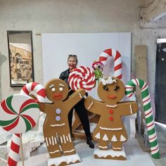 a woman standing next to two giant gingerbread men with candy canes in their hands