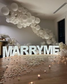 the word marry me is surrounded by white balloons and confetti in front of it