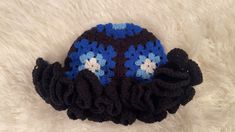 a crocheted hat with blue and white flowers on it sitting on a furry surface