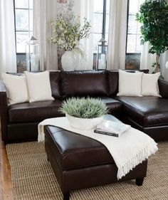 a living room with brown leather couches and white pillows on top of the rug