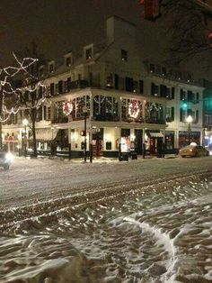 a city street is covered in snow during the night time with christmas lights and decorations