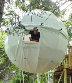 a man standing in the middle of a tree with a white tent on top of it