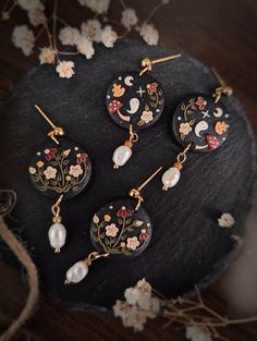 four pieces of jewelry sitting on top of a wooden table next to flowers and leaves