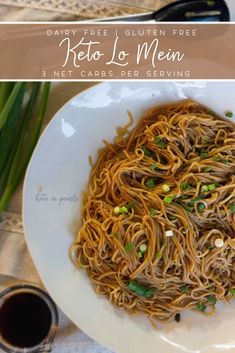 a white plate topped with noodles next to chopsticks and green onions on a table