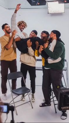 a group of men standing around each other in front of a white wall and black chairs