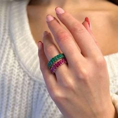 a woman's hand holding a ring with three different colored stones on the band