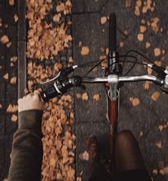 a person riding a bike with their feet on the handlebars in front of autumn leaves