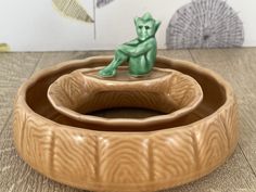 a small green toy sitting on top of a wooden bowl